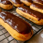 Rad domácich éclairs s maslovým krémom a čokoládovou polevou elegantne uložených na podnose.